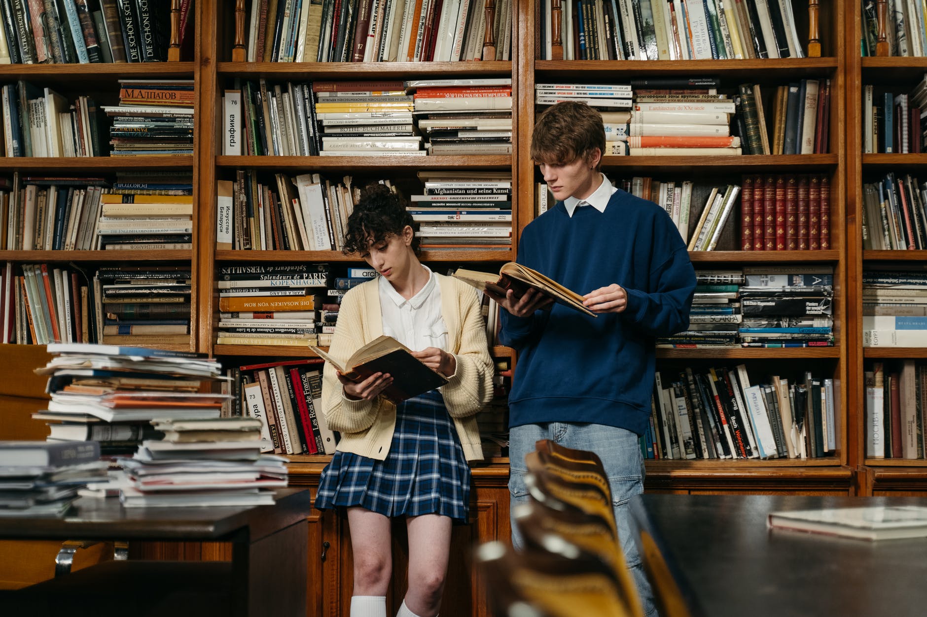 a man and a woman reading books while leaning on a bookcase